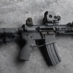 Photo of a short barreled ar15 556 rifle black and gray tones laying on a dark marble table with subtle grain texture