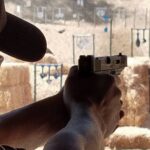 man with ear protection at an outdoor range shooting a small caliber pistol chambered in 9mm at steel targets in the midwest mountains
